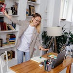 A young woman with earphones video conferencing from her home office surrounded by books.